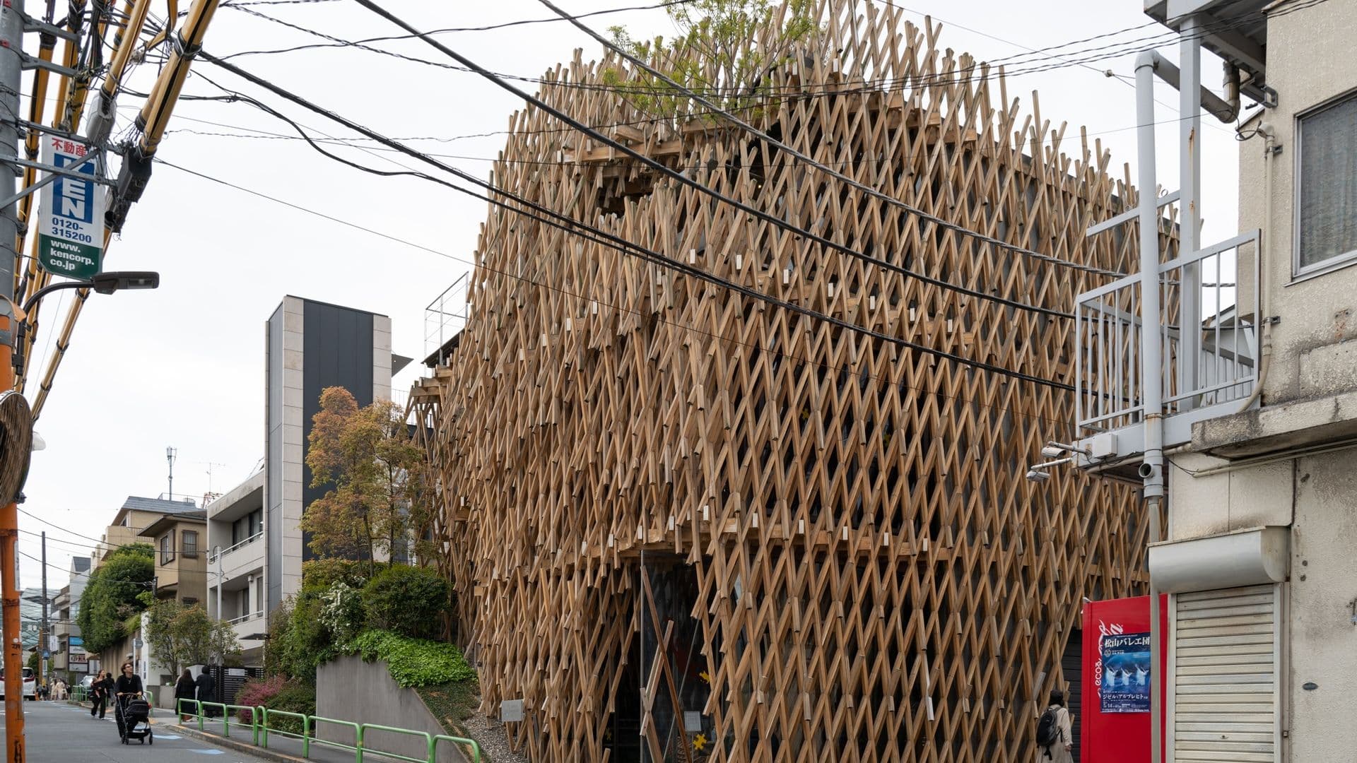 Modern building with a unique wooden lattice facade on a city street with pedestrians and utility wires.