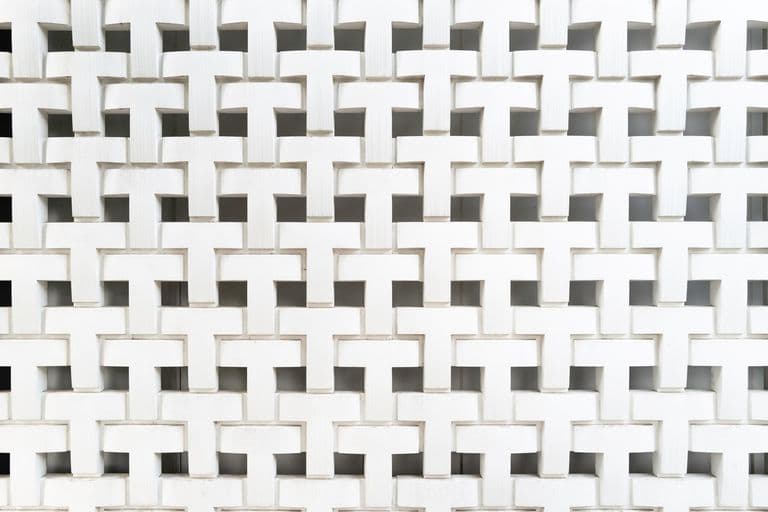 White geometric facade with repeating T-shaped cutouts arranged in a grid pattern.