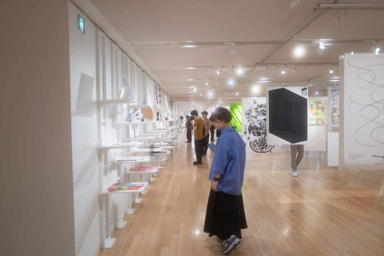 People viewing modern art and design pieces in an art gallery or exhibition space.
