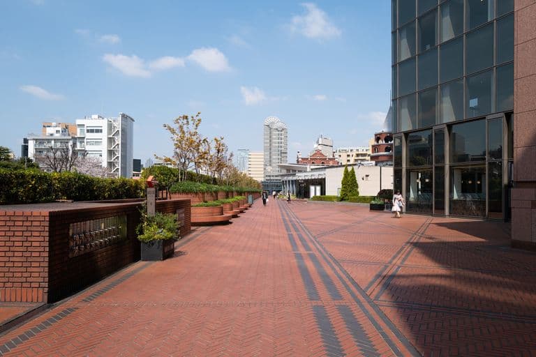 Urban outdoor walkway with brick pavement and modern buildings under a blue sky.