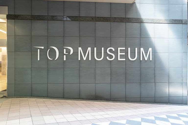 Sign on exterior wall of a museum that reads 'TOP MUSEUM' with a partially obscured letter 'T' and the rest of the letters visible, mounted on a tiled wall.