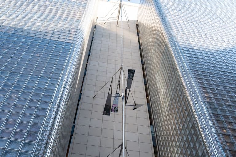 View of two tall, modern glass skyscrapers with a cow sculpture extending between them, seen from ground level looking up.