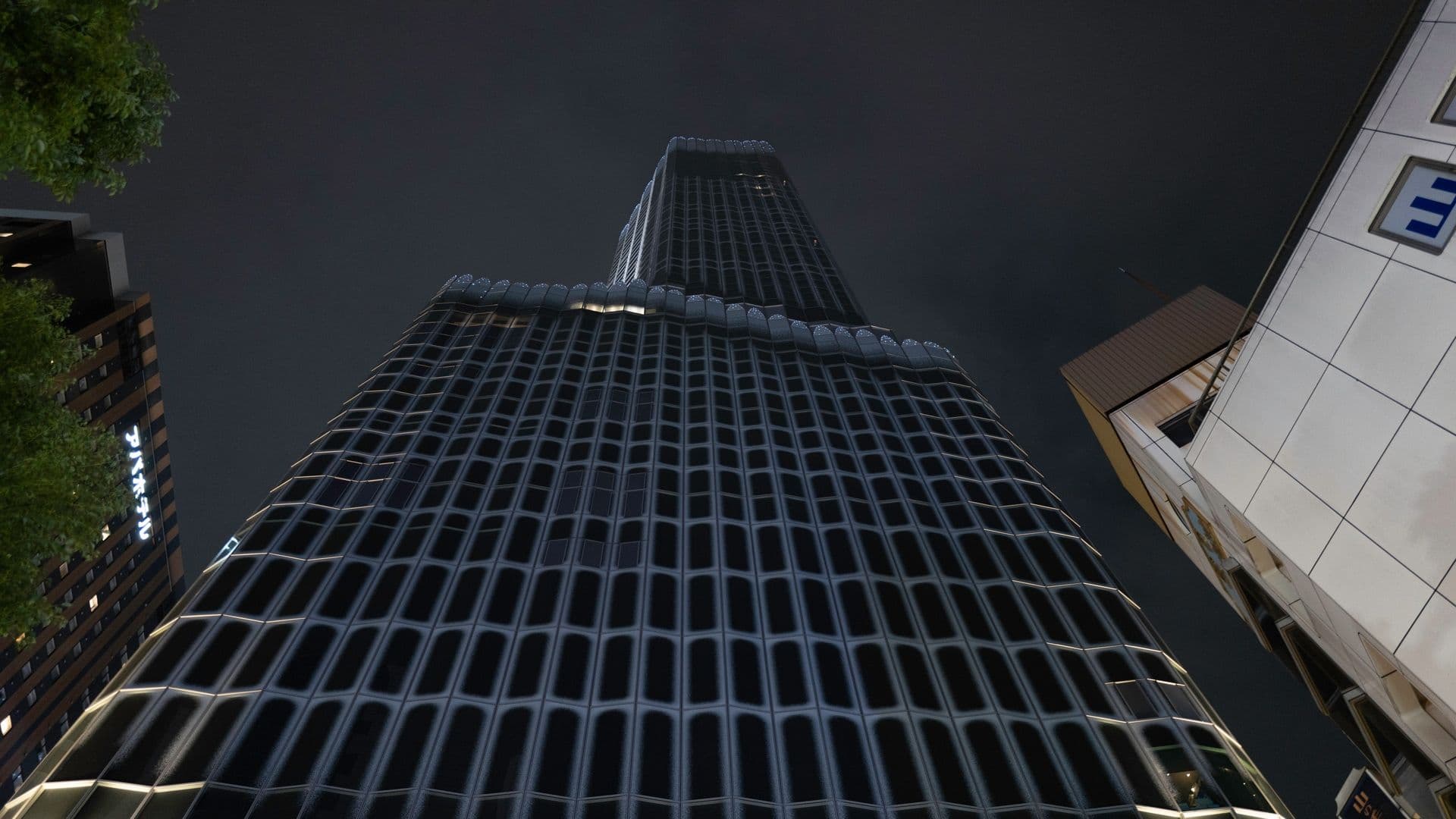Low-angle view of a tall, modern skyscraper at night with illuminated windows and a unique grid-like facade, surrounded by other buildings.