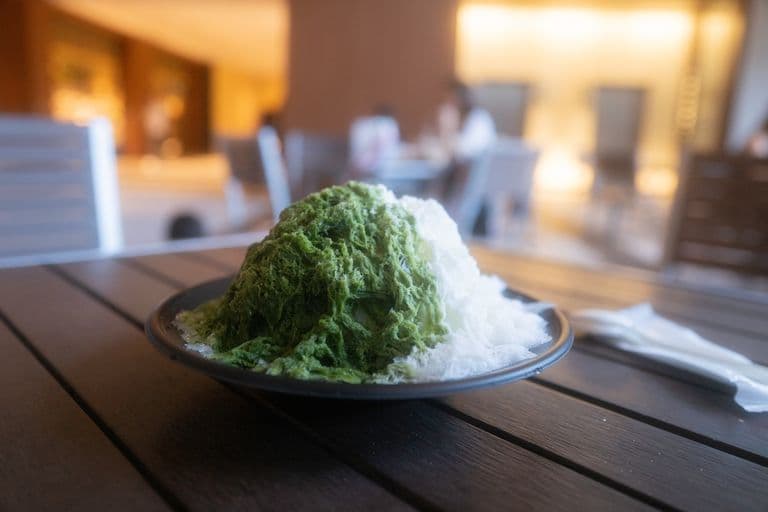 Plate of green and white shaved ice dessert on wooden table in a restaurant setting.