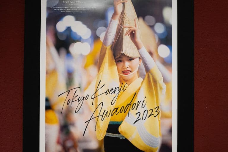 A festival poster displays a woman in a yellow kimono with a traditional woven hat, holding a conical straw hat above her head in a nighttime festival scene with blurred lights in the background. The poster reads 'Tokyo Kamei Awadori 2023' and features Japanese characters and event dates.