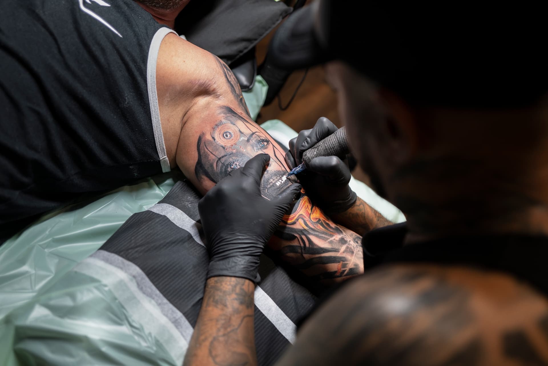 Tattoo artist creating a colorful tattoo on a man's arm in a tattoo studio.