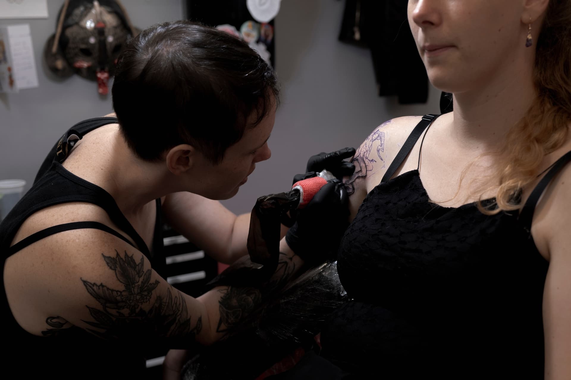 Tattoo artist tattooing a woman on her shoulder in a tattoo studio.