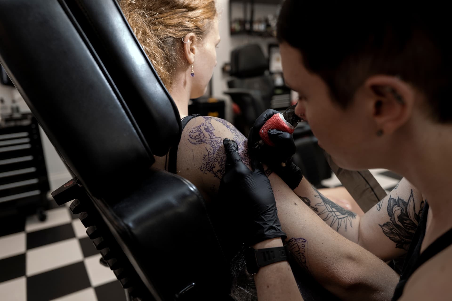 Tattoo artist tattooing a person’s arm receiving tattoo in tattoo shop.