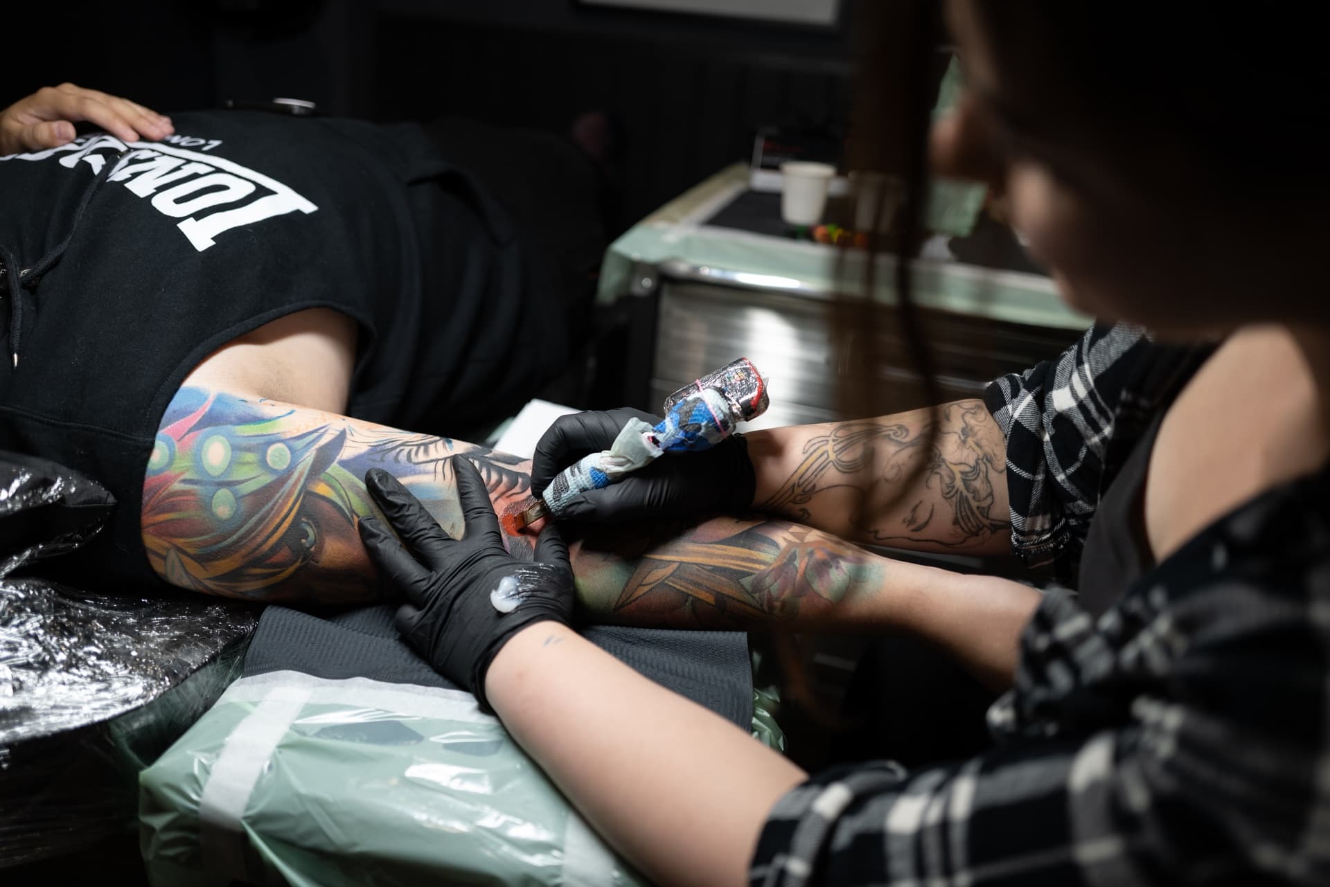 A tattoo artist is tattooing a colorful sleeve on a person's arm.