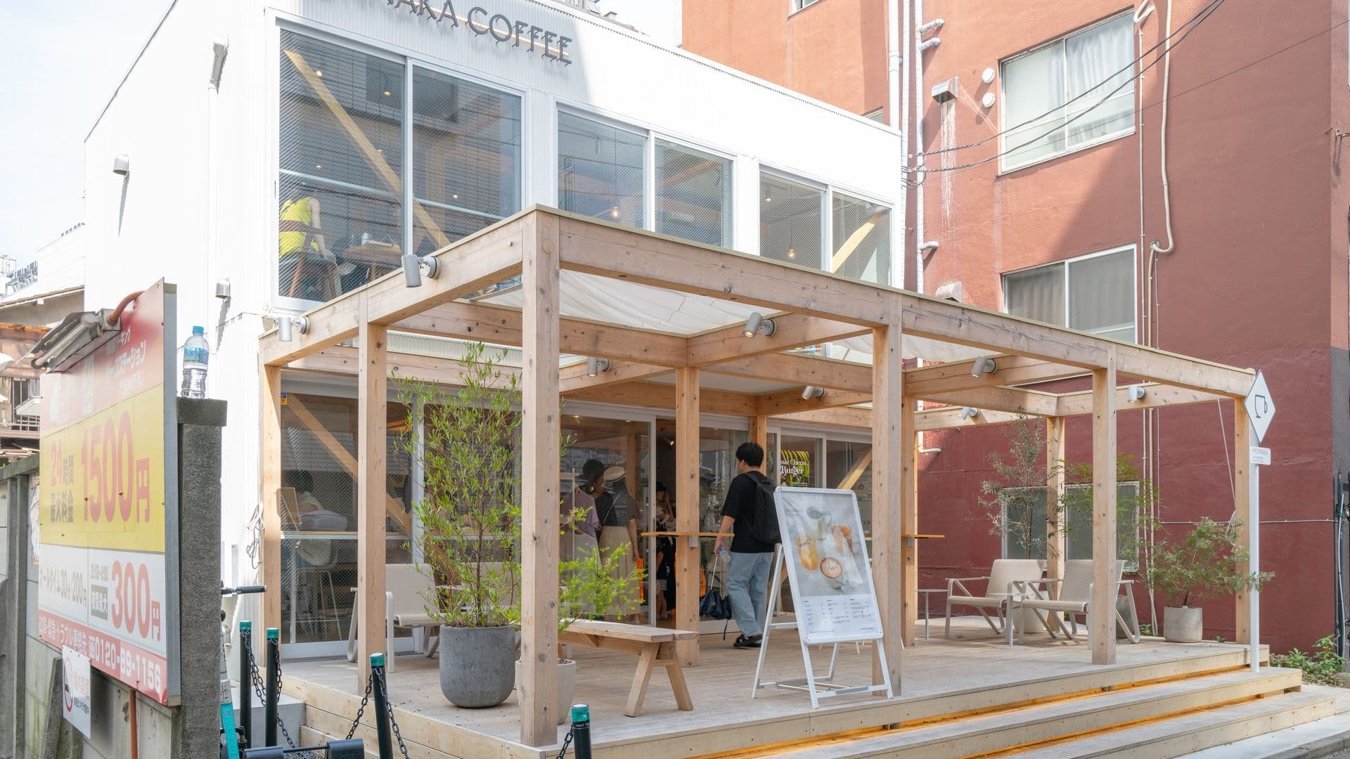 Exterior view of Monnaka Coffee shop with a wooden patio and seating area, people entering, and signage on the building.