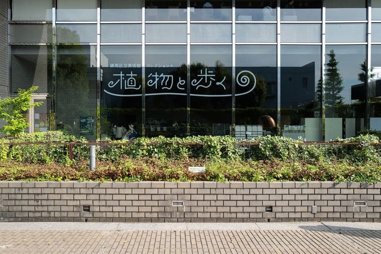 A modern glass building with Japanese characters and a spiral design on the front window, surrounded by greenery and a brick sidewalk.