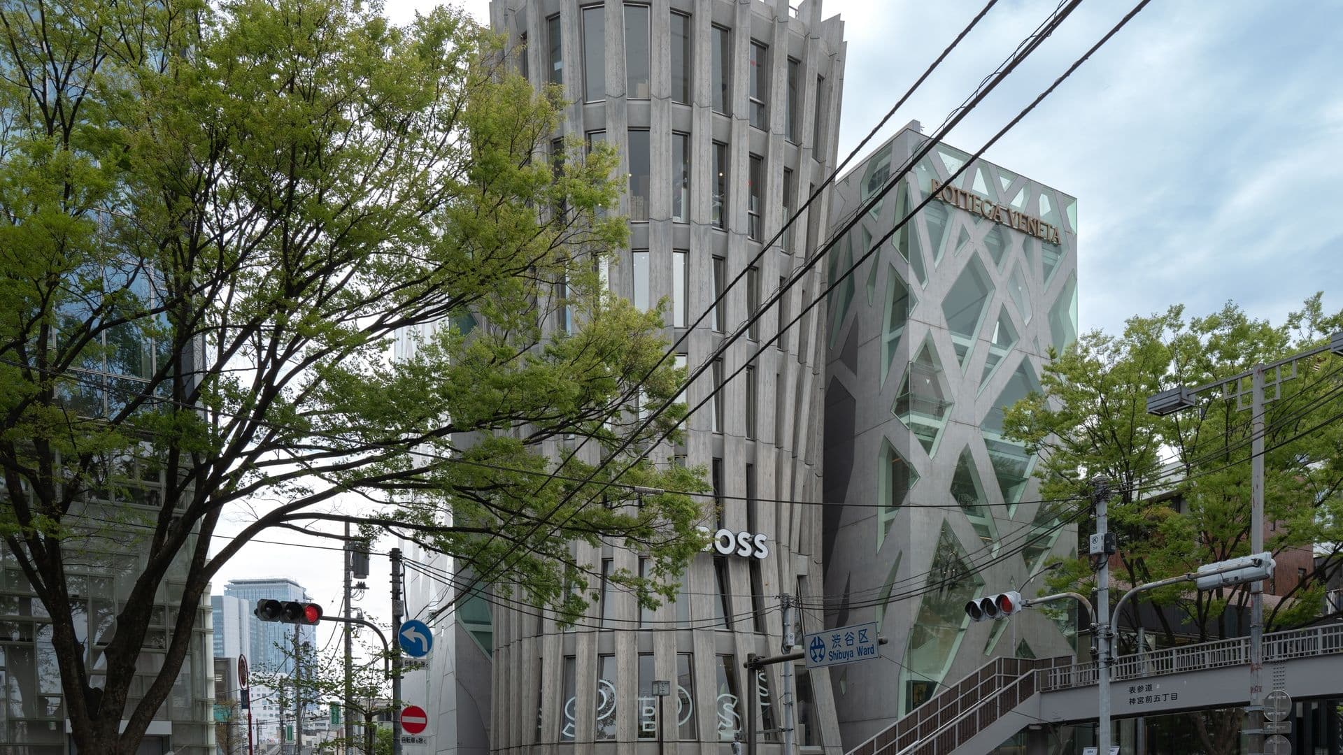 Street scene in Tokyo with modern building, trees, cars, bicycles, and pedestrians.