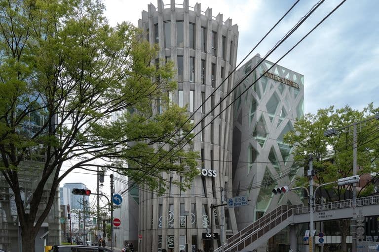 Modern multi-story building with unique architectural design, surrounded by trees at street intersection in urban setting