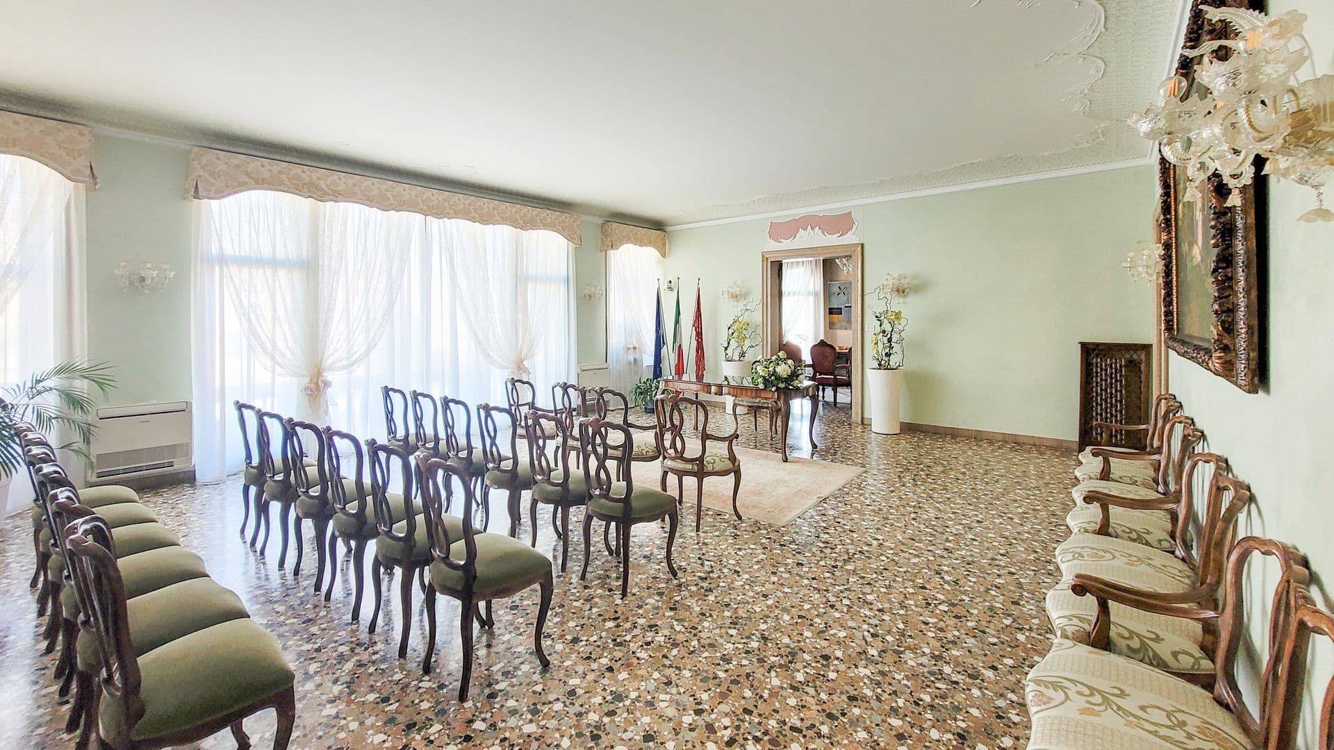 Elegant conference room with chairs arranged around a central table, large windows with sheer curtains, decorative ceiling molding, and ornate lighting fixtures.