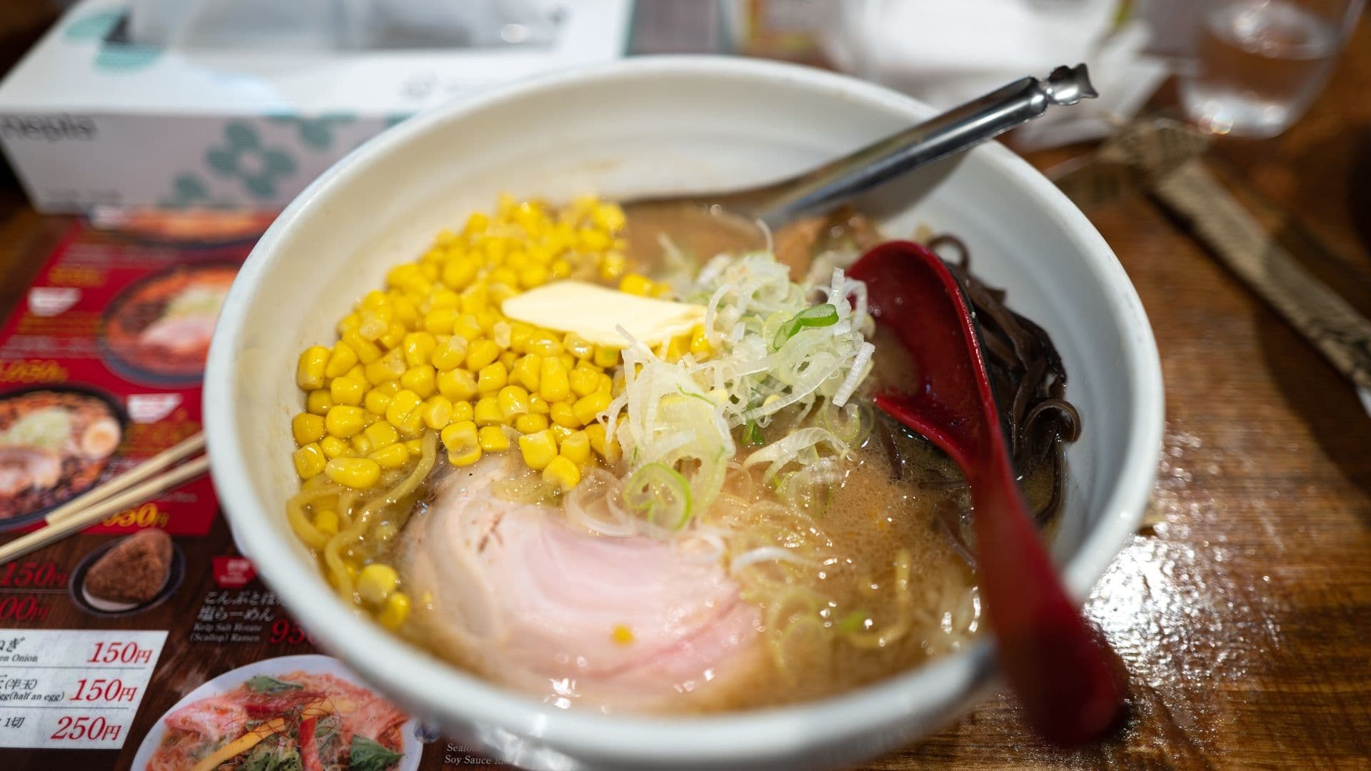A bowl of ramen with corn, sliced pork, green onions, seaweed, and a pat of butter