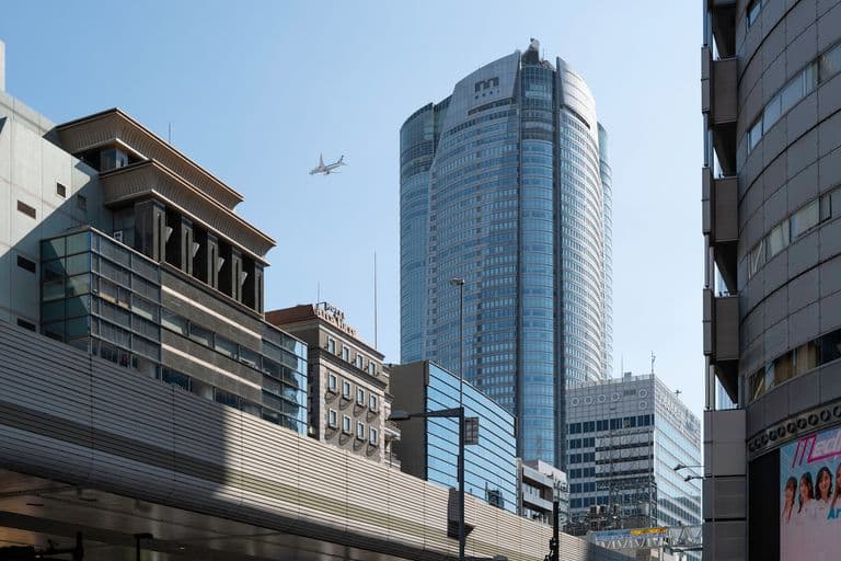 A cityscape with tall modern buildings and an airplane flying in the clear blue sky.