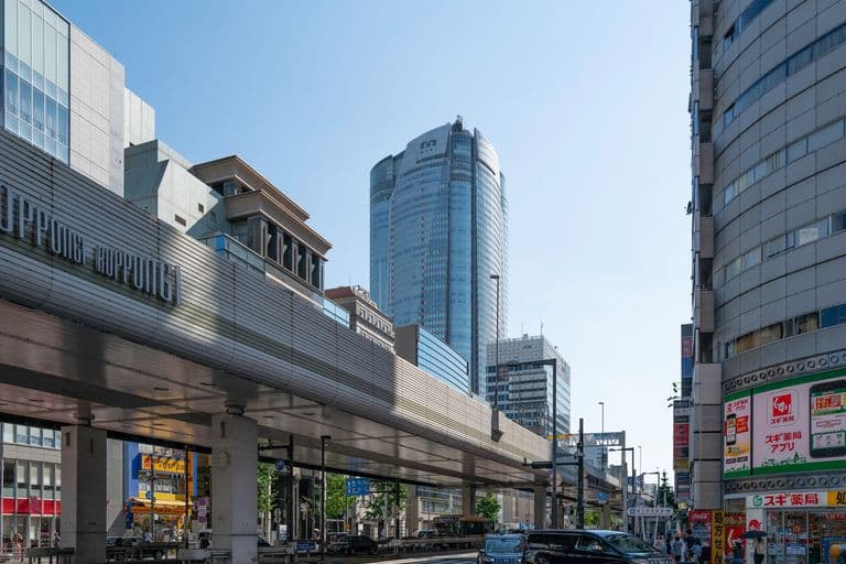 City street scene with tall modern buildings, an elevated train track, and busy street traffic.