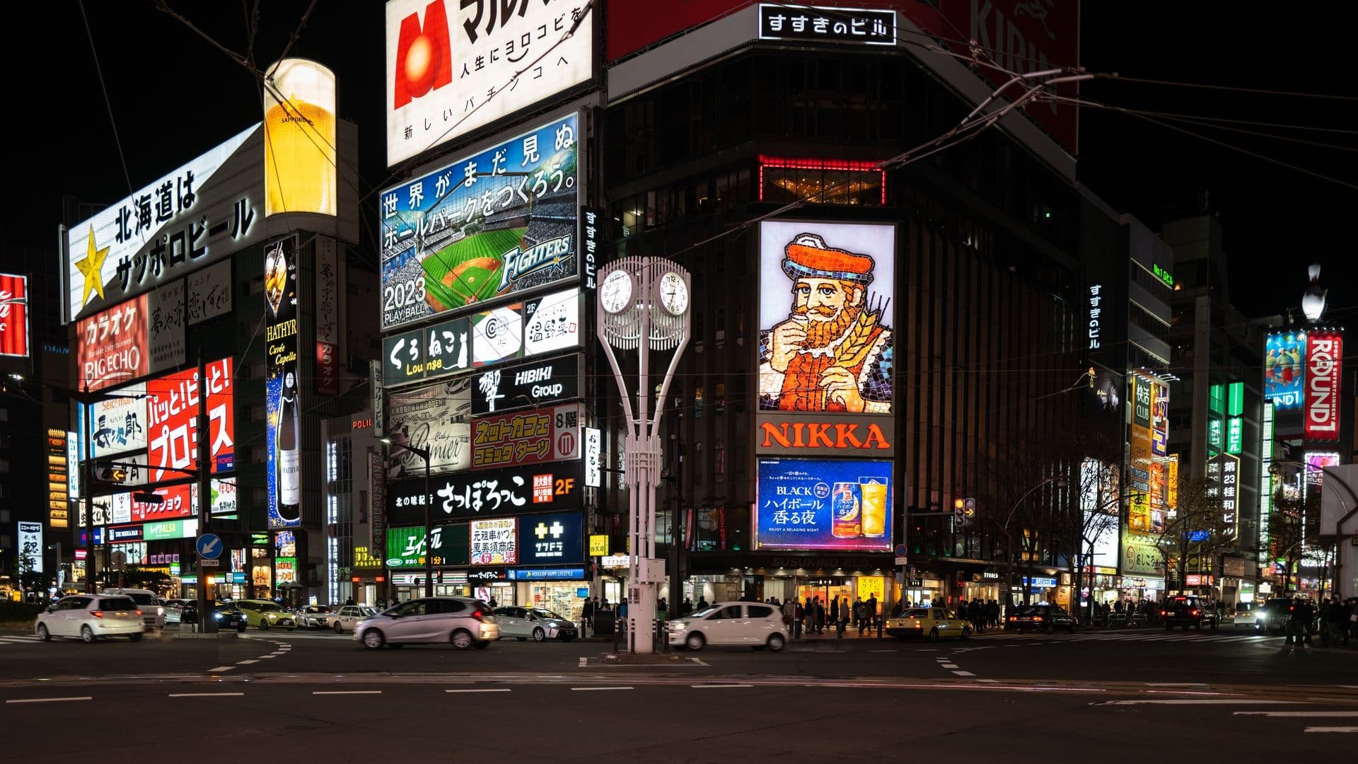Night scene at Sapporo's Susukino district with vibrant neon signs and electronic billboards, including prominent Nikka Whisky signage and various advertisements in Japanese.