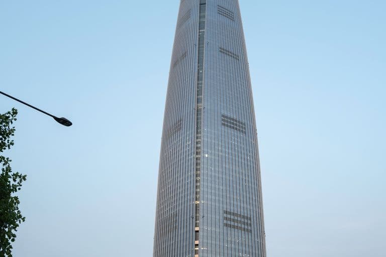 Tall skyscraper called Lotte World Tower in Seoul, South Korea, with a modern base and busy street with cars and buses at its foot.