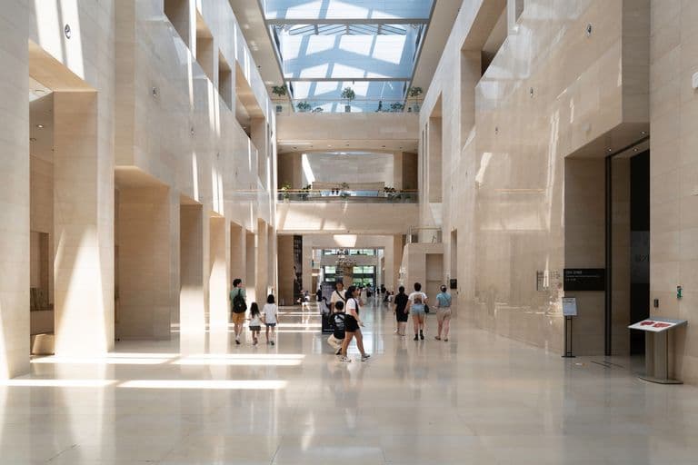 Interior of a modern museum with high ceilings, natural light, and visitors walking around.