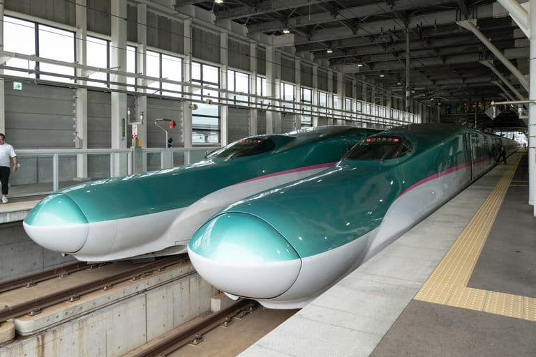 Two bullet trains parked inside a train station with large windows, grey walls, and a corridor.