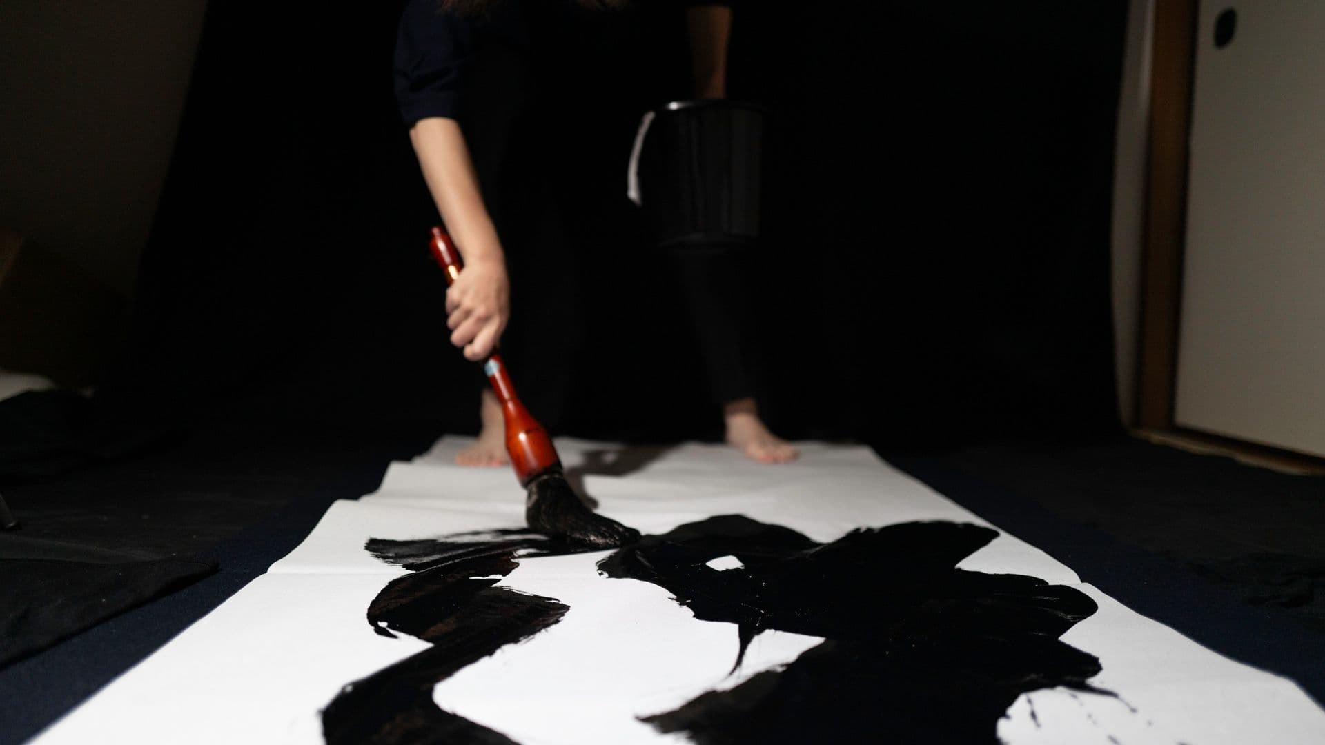 Person painting large black calligraphy on white paper with brush