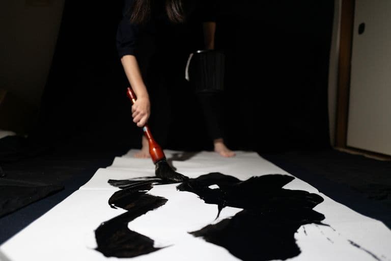 Person painting large black calligraphy on white paper with brush