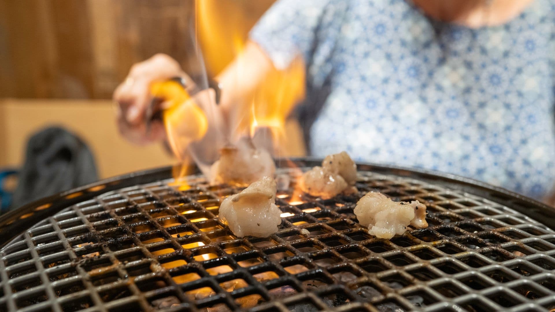 Person grilling pieces of meat over an open flame on a wire mesh grill.