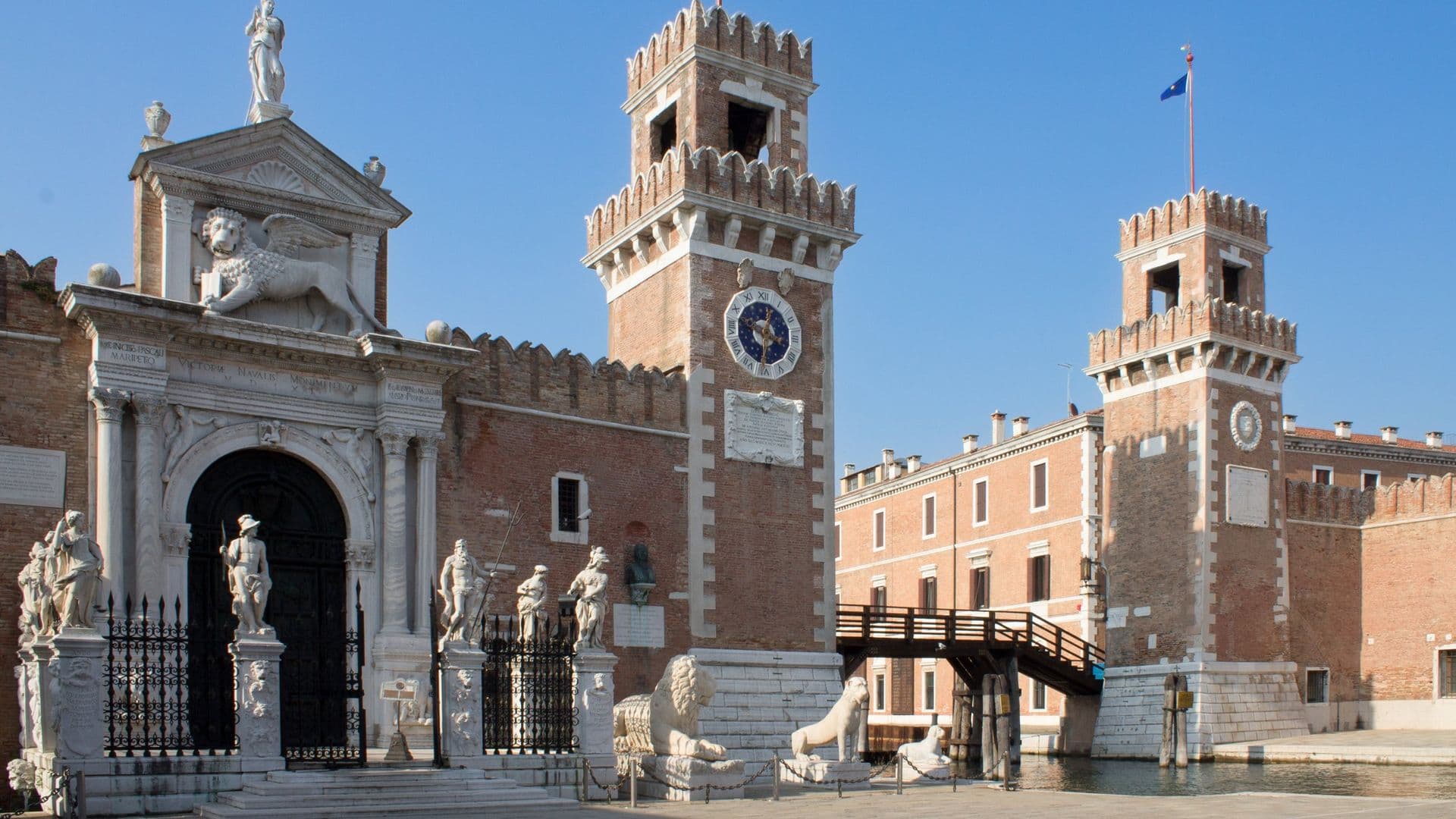Entrance of Venetian Arsenal with two brick towers, statues, and lion sculptures in Venice, Italy.