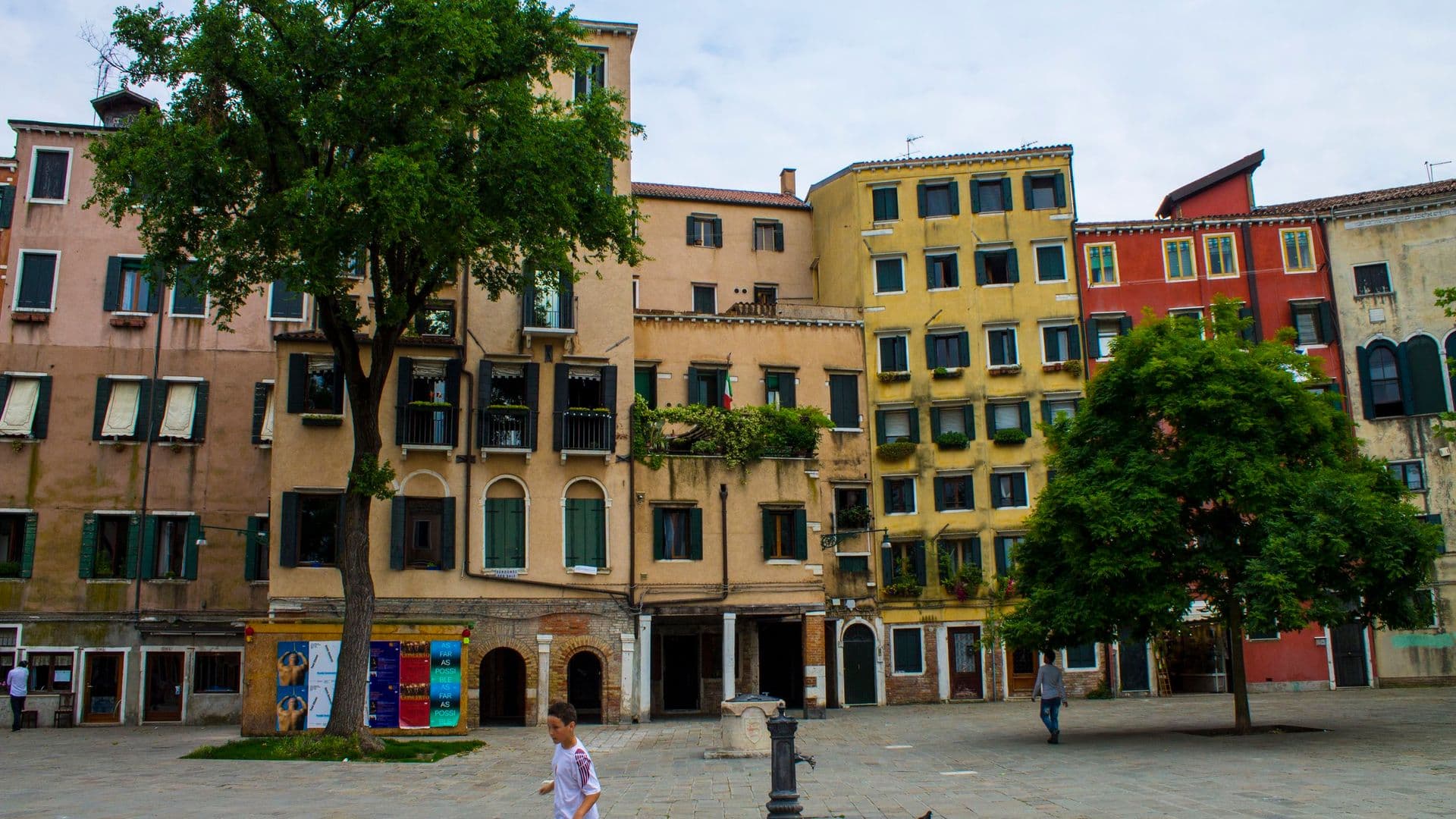 Scenic view of a quiet square with historic European buildings, trees, and a couple of people walking.
