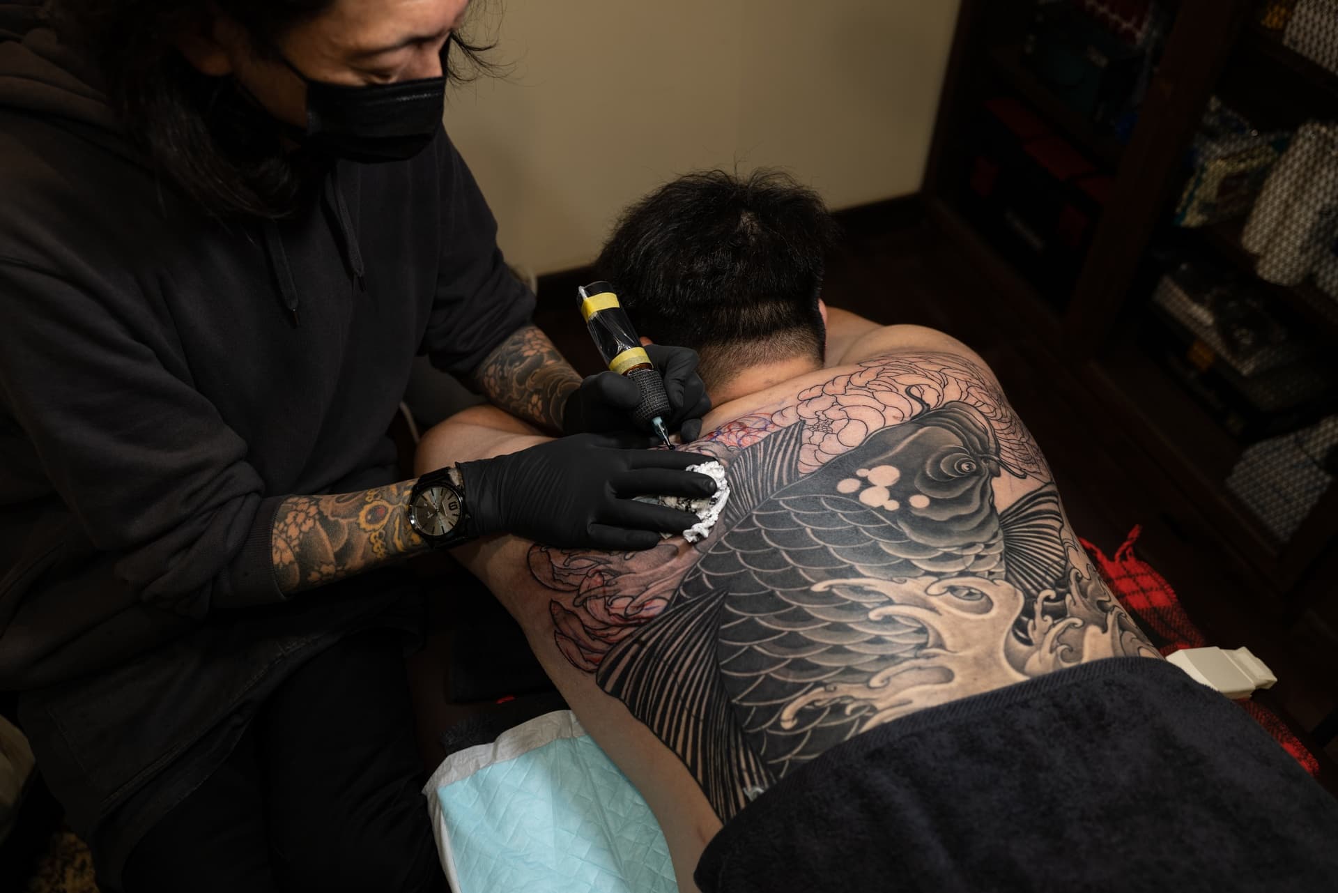 Tattoo artist working on a large Japanese-style tattoo of a koi fish on a person's back.