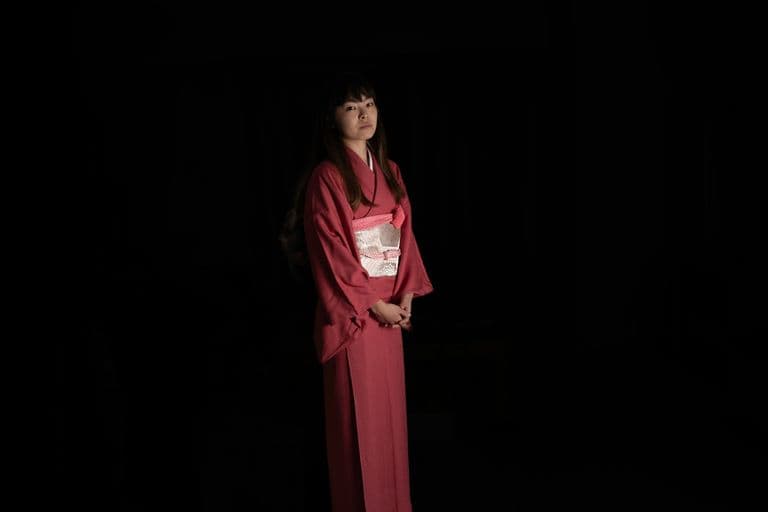 Woman wearing a traditional kimono in a dimly lit room.
