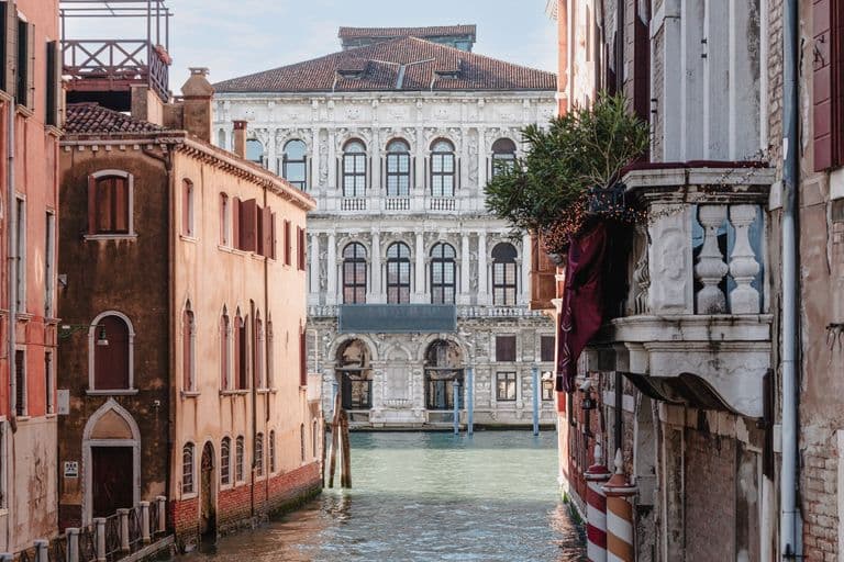 View of a canal in Venice, Italy, with historic buildings on both sides and a large ornate building in the background.
