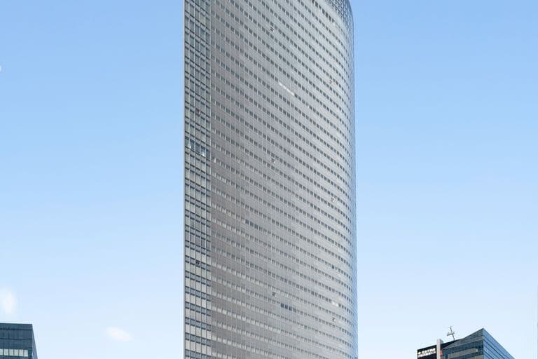 Tall modern glass skyscraper with curved design in a cityscape, other high-rise buildings around, clear blue sky.