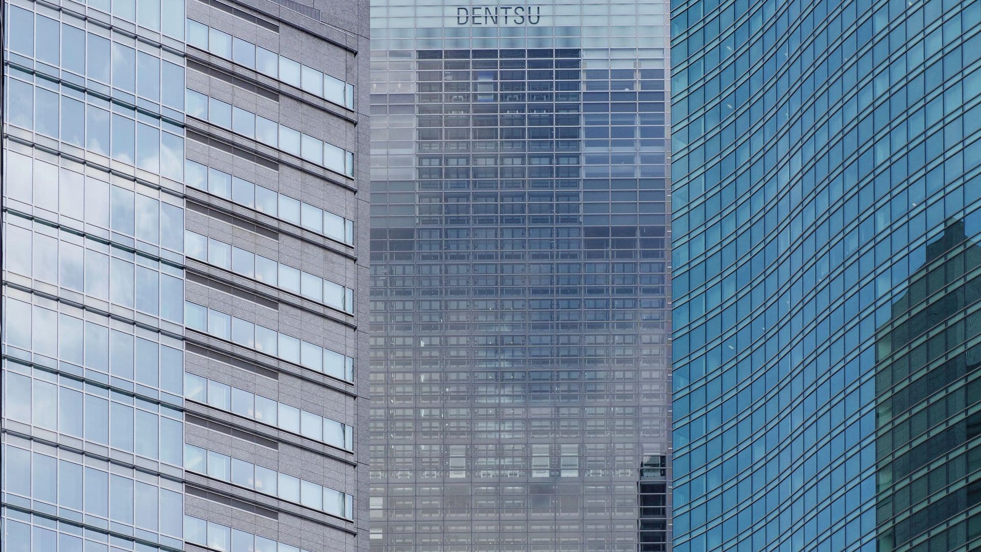 Close-up of modern skyscrapers with glass windows, one with the 'DENTSU' logo at the top.