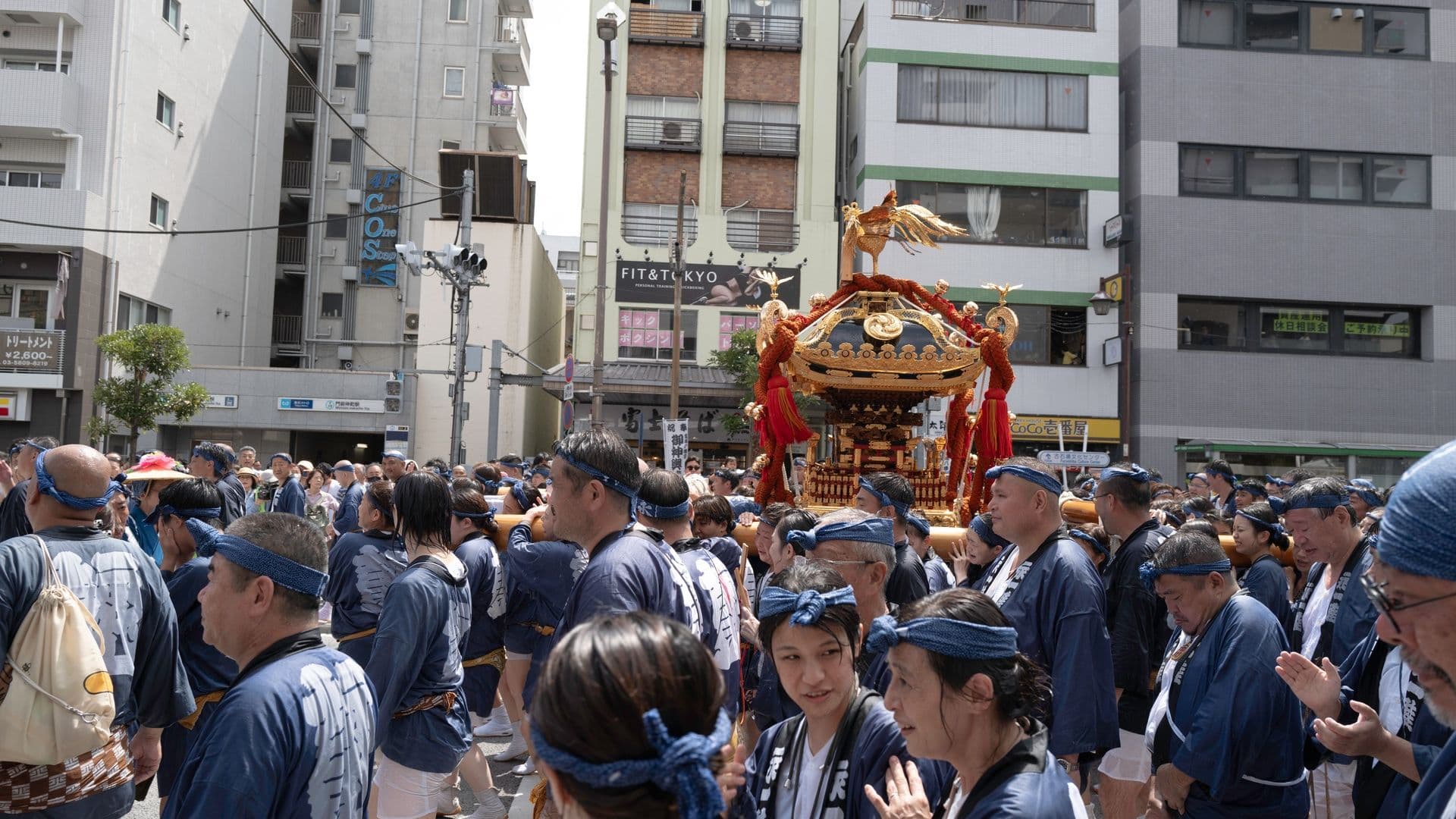 People participating in a traditional Japanese festival parade, carrying a decorated wooden float through city streets.