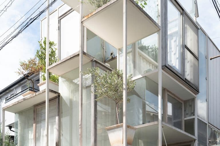 Modern multi-story building with glass balconies and potted plants, parked vintage car underneath