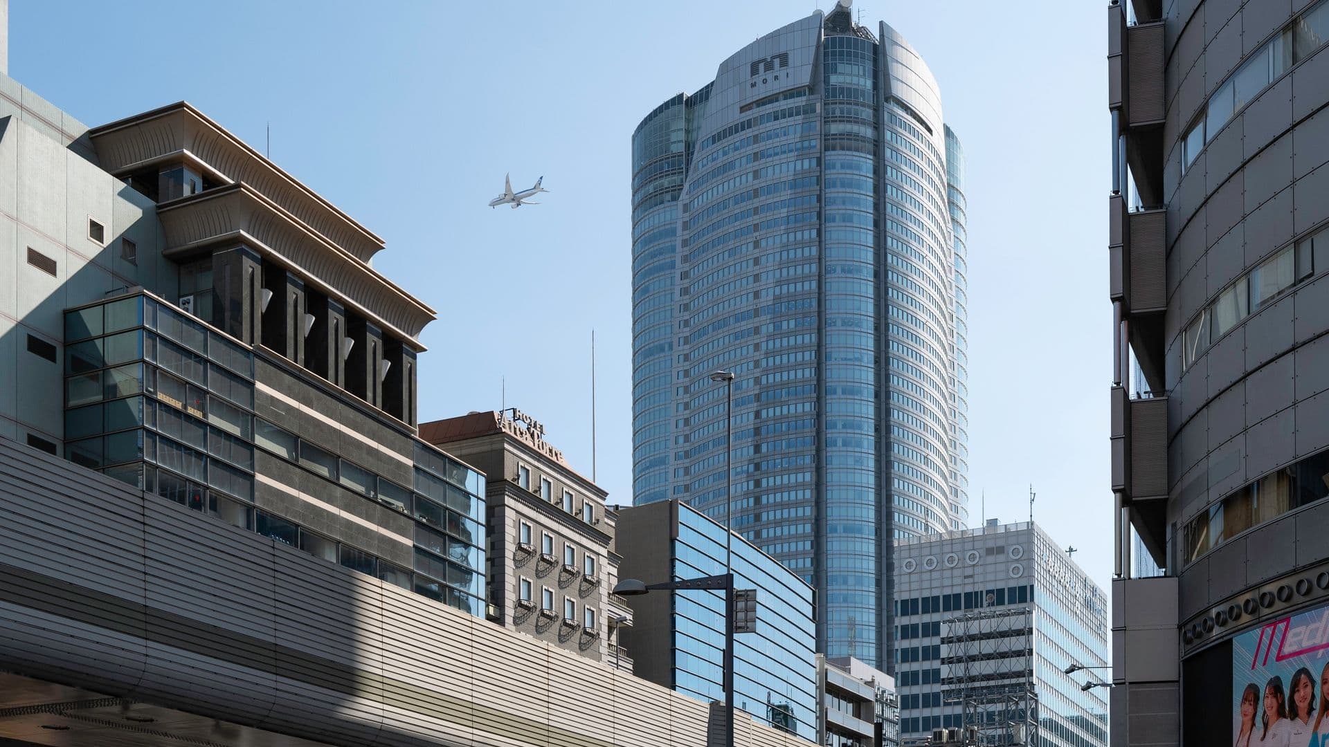 Cityscape with tall modern skyscrapers, an airplane flying in the clear blue sky, and urban buildings in the foreground.