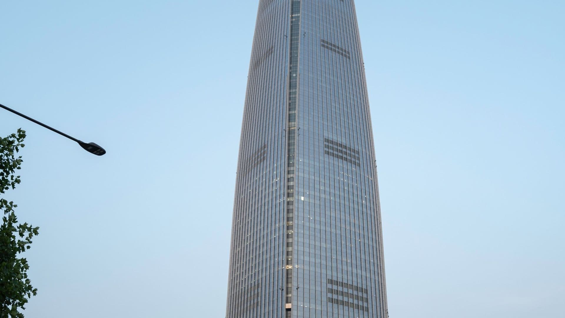 The Lotte World Tower, a tall skyscraper, standing against a clear sky in Seoul, South Korea, with a busy street and shopping mall at its base.