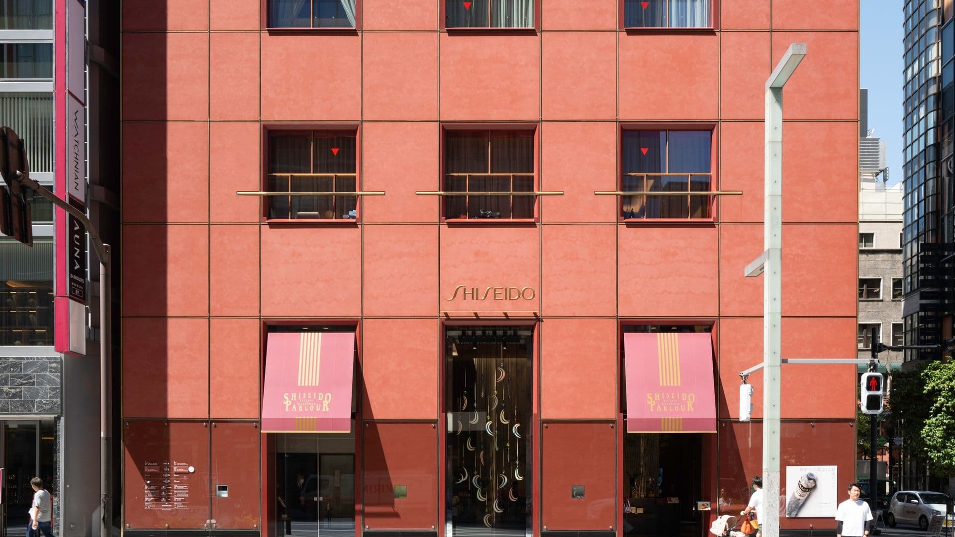 Shiseido store on a city street with pink exterior, pink banners, and pedestrians walking by.
