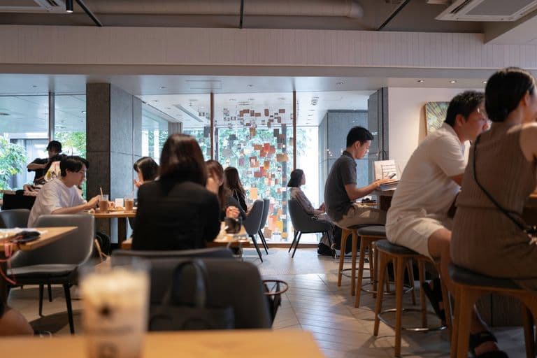 People dining and working at a cafe with natural light, modern decor, and a colorful art installation in the background.