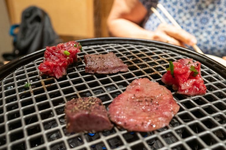 Various pieces of raw meat with green onions on a grill at a restaurant.