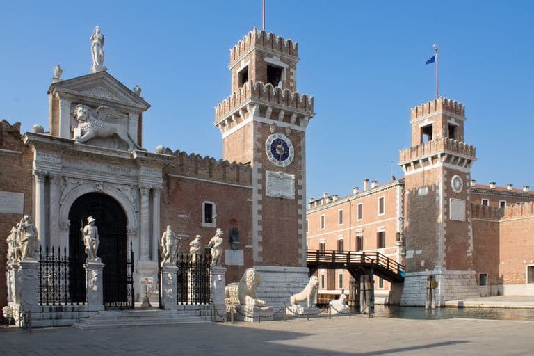 Entrance of Venetian Arsenal with two brick towers, statues, and lion sculptures in Venice, Italy.