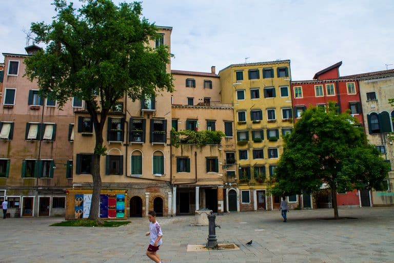 Scenic view of a quiet square with historic European buildings, trees, and a couple of people walking.