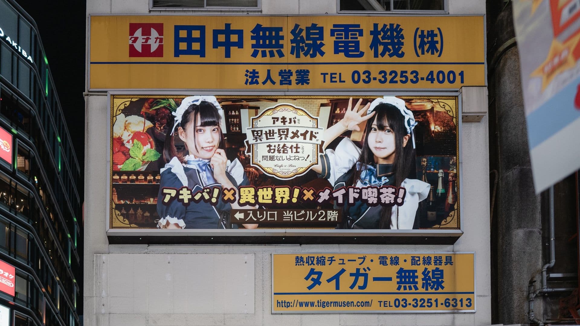 A billboard showing two women dressed as maids in a cafe, with Japanese text around them and a café interior background.
