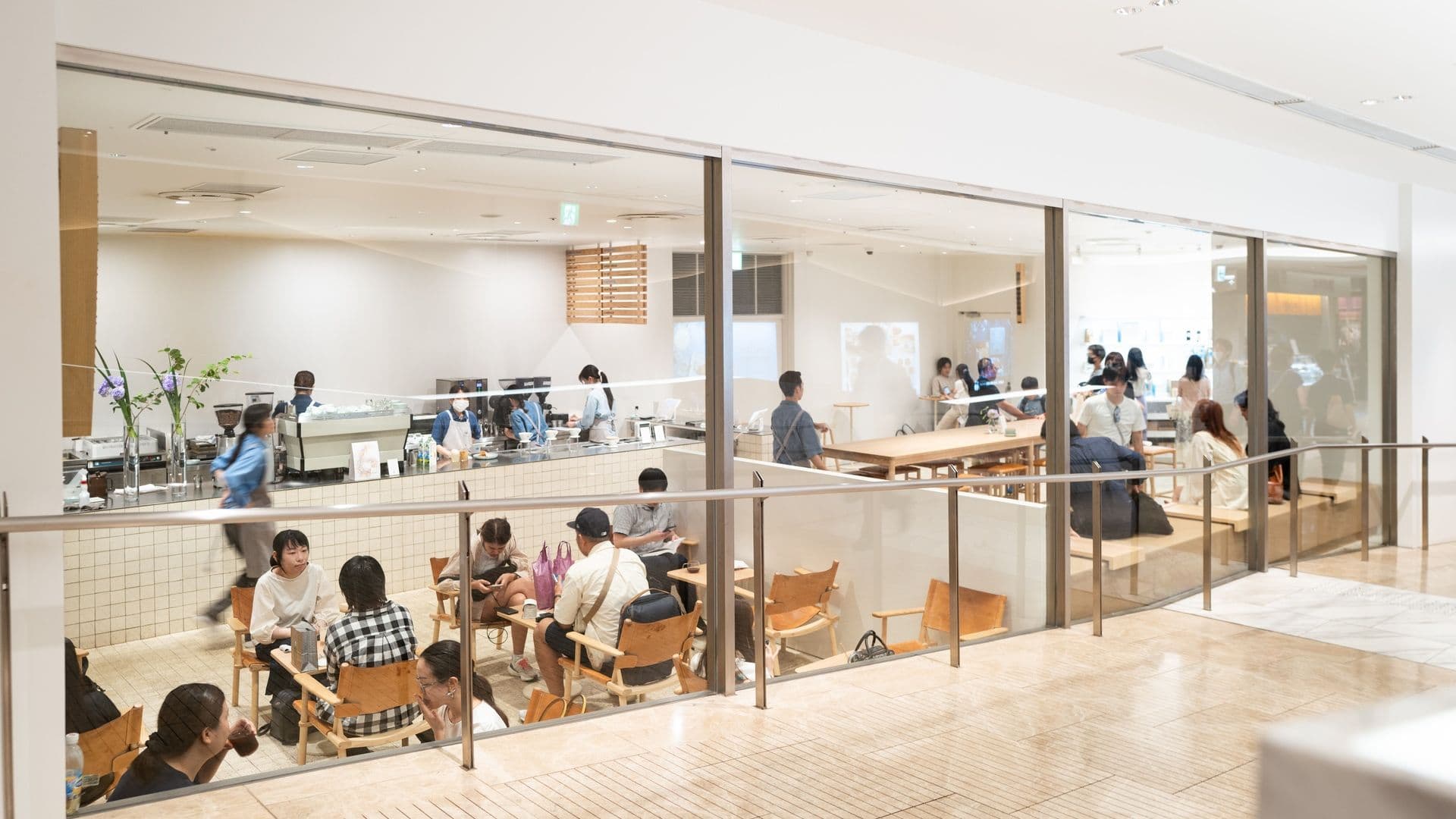 Inside a modern cafe or coffee shop with customers sitting at tables and a counter with baristas making drinks.
