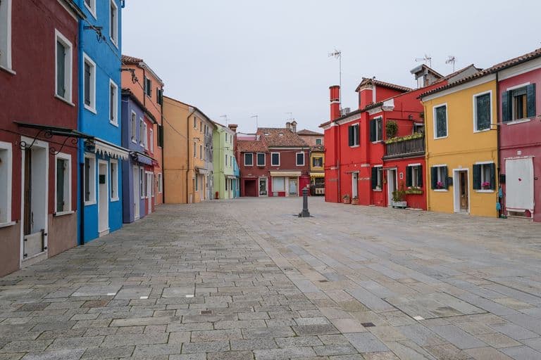 Colorful buildings lining a cobblestone street in a small European town, with mostly overcast sky.