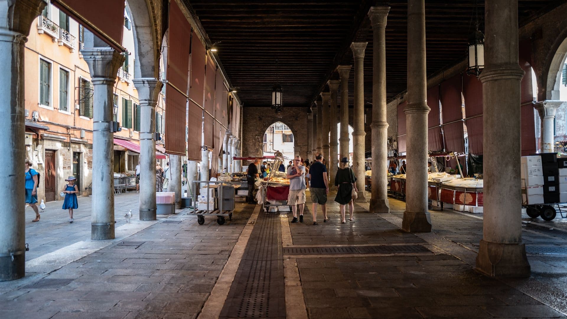 Interior of an open-air market with arched columns and people walking.