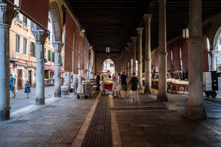 Interior of an open-air market with arched columns and people walking.